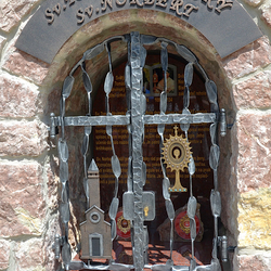 Kovaný pamätník s atribútmi svätých. Sv. Tomáš Akvinský - kostol, Sv. Norbert - monštrancia